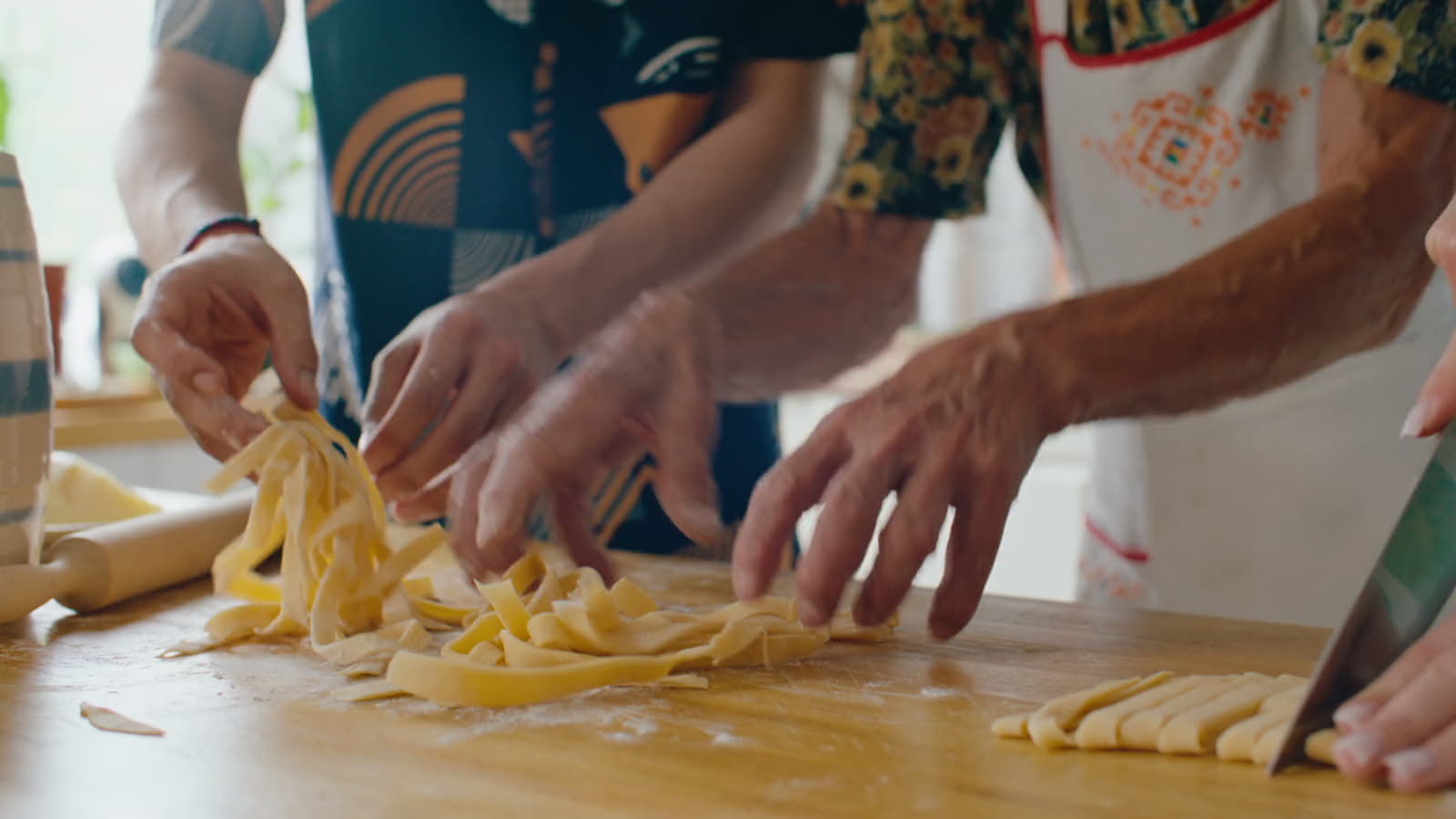 Hands cutting fresh tagliatelle on a floured board