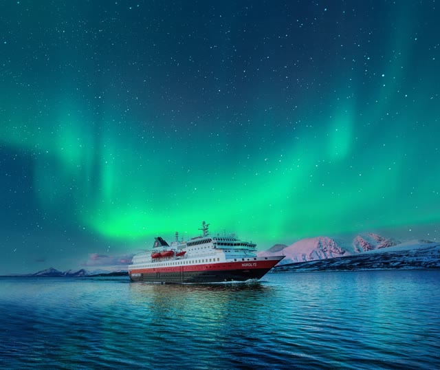 The coastal ship on still Arctic water under green ribbons of the aurora borealis