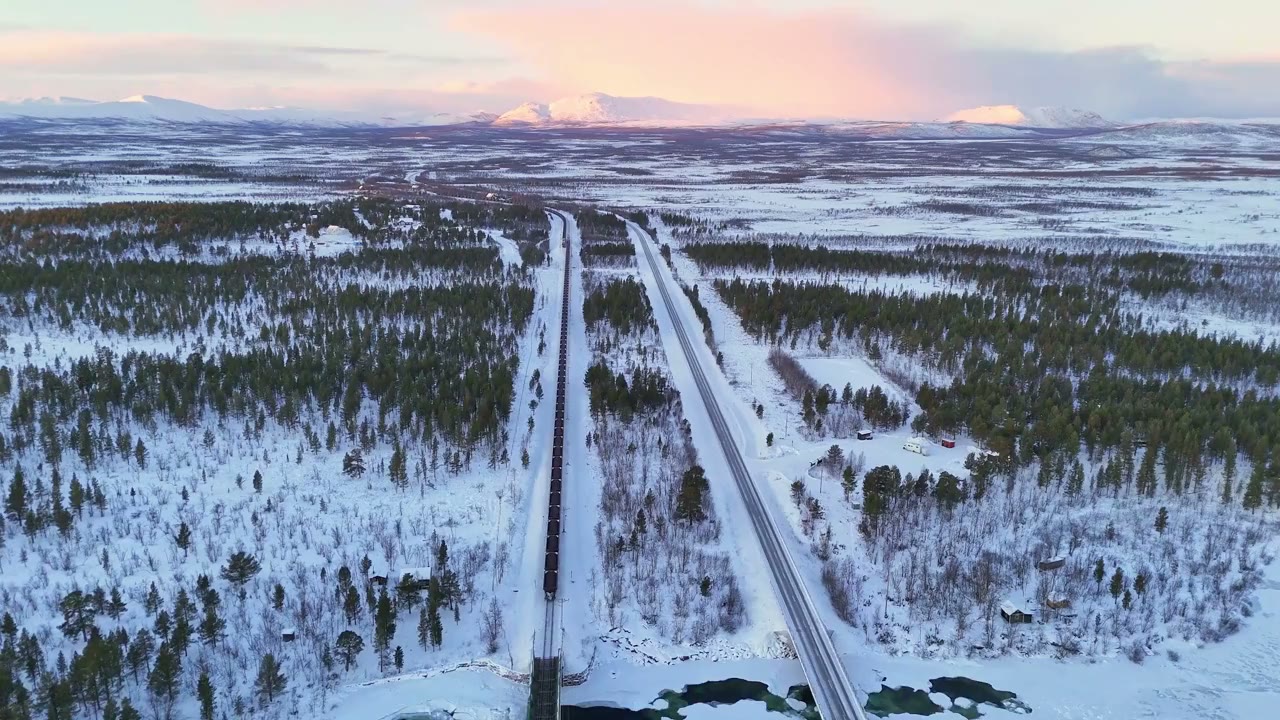 The iron-ore railway and the winter road side by side through snow-covered forest at polar sunset