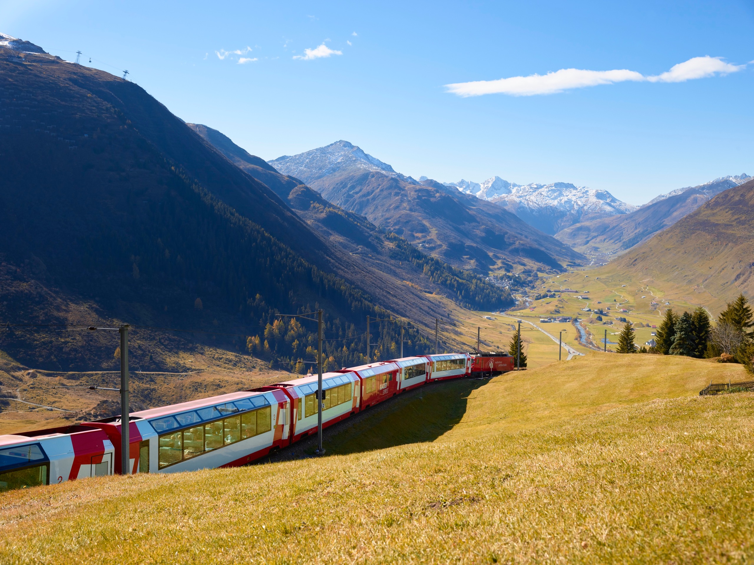 The Glacier Express curving through the Andermatt valley beneath snow-capped peaks