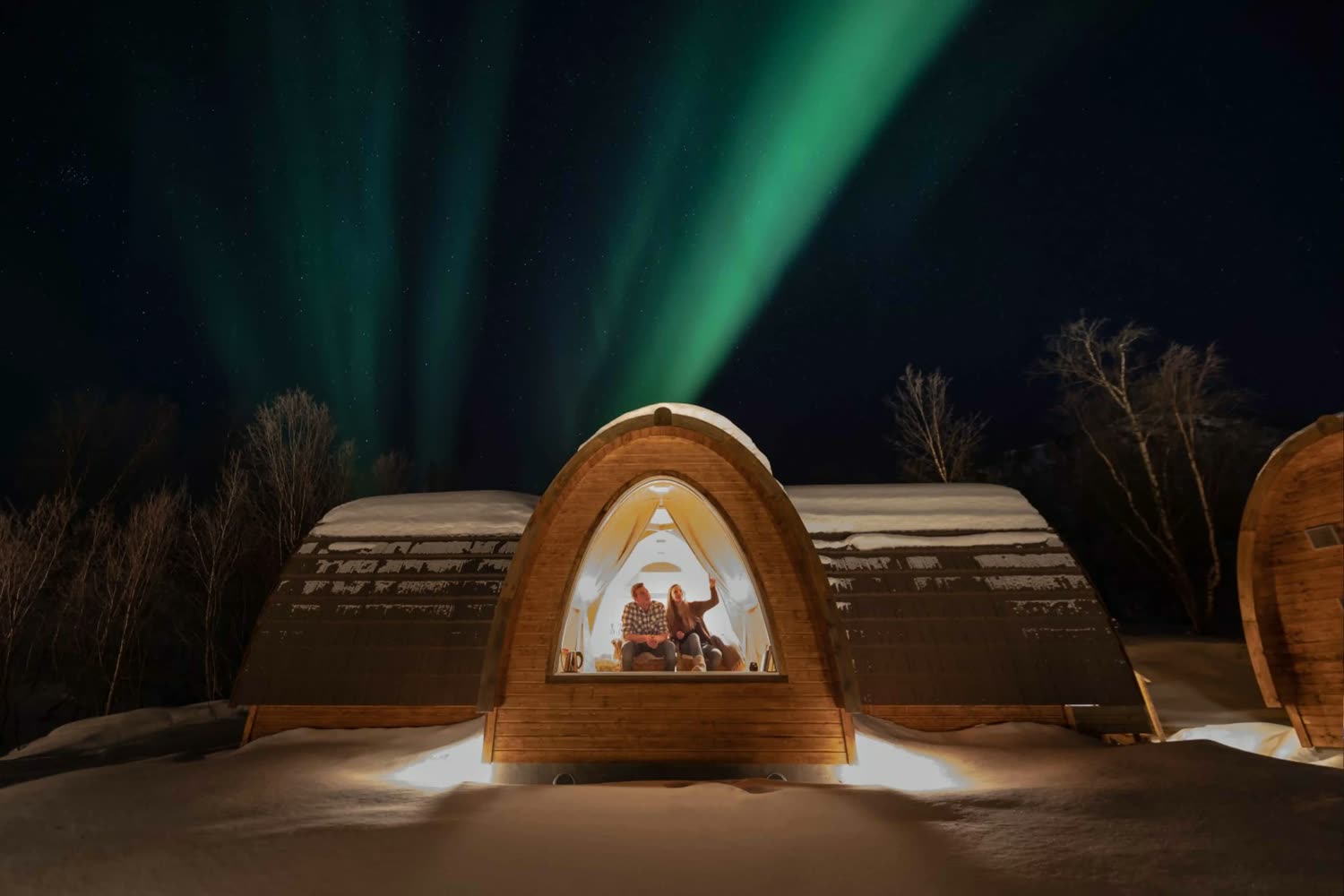 A lit Gamme cabin at Snow Resort Kirkenes under the northern lights